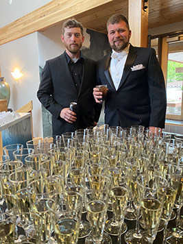 Two men posing by the champagne glasses at the gala
