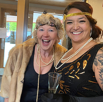 Two smiling ladies dressed in 1920's costumes posing for a picture at the gala