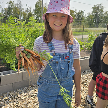 Happy female student holding a bunch of freshly picked carrots